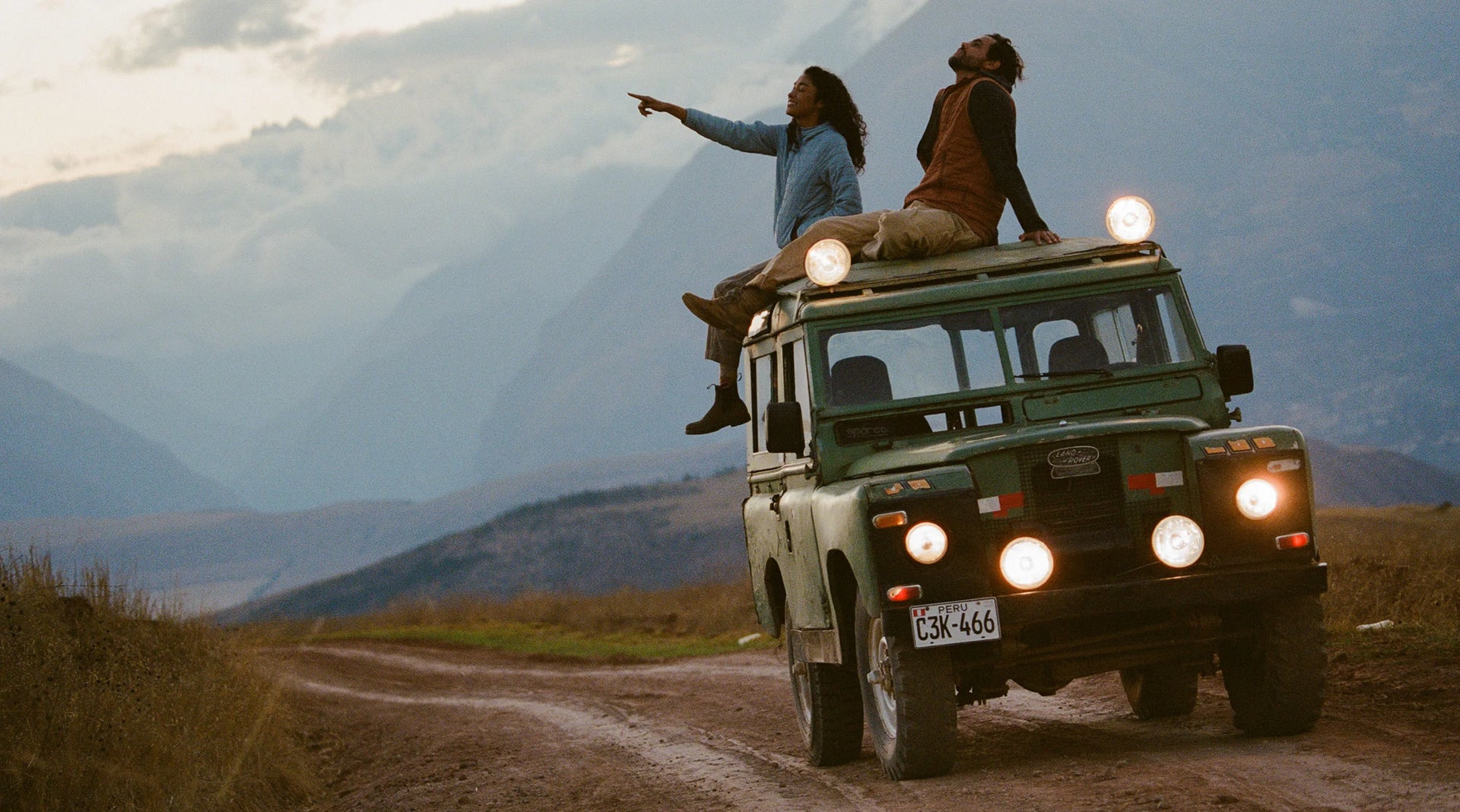 Load video: Video of man and woman sitting on top of an old jeep on a dirt road in Peru wearing Mayu Ultralight apparel