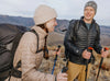 Two hikers on a mountain trail, woman in a beige slim-fit insulated jacket and man in a black ultralight insulated jacket