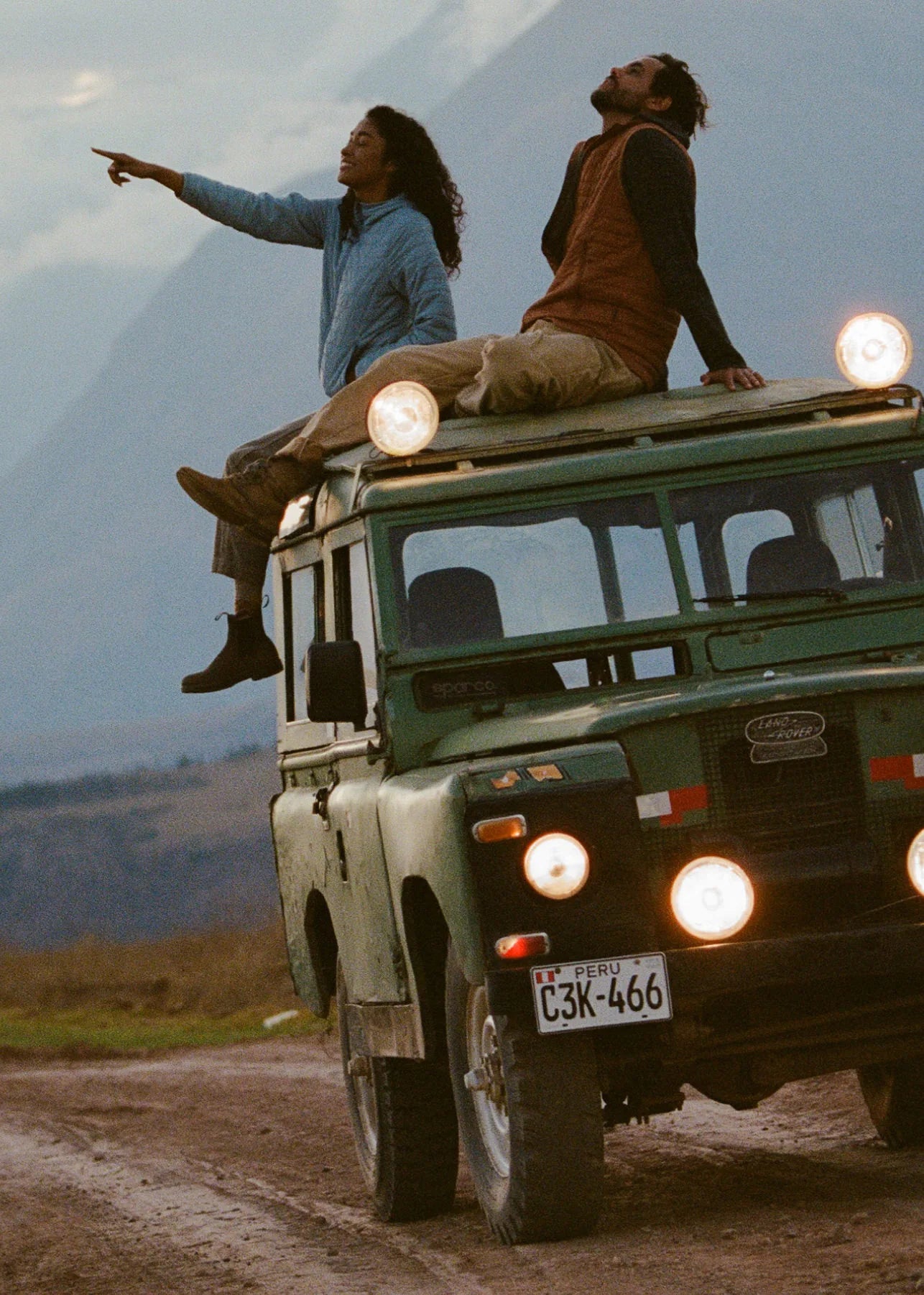 Load video: Video of man and woman sitting on top of an old jeep on a dirt road in Peru wearing Mayu Ultralight apparel