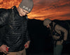 Three-quarter view of Mayu Ultralight jacket showing lightweight puffer quilting and hood against a sunset sky