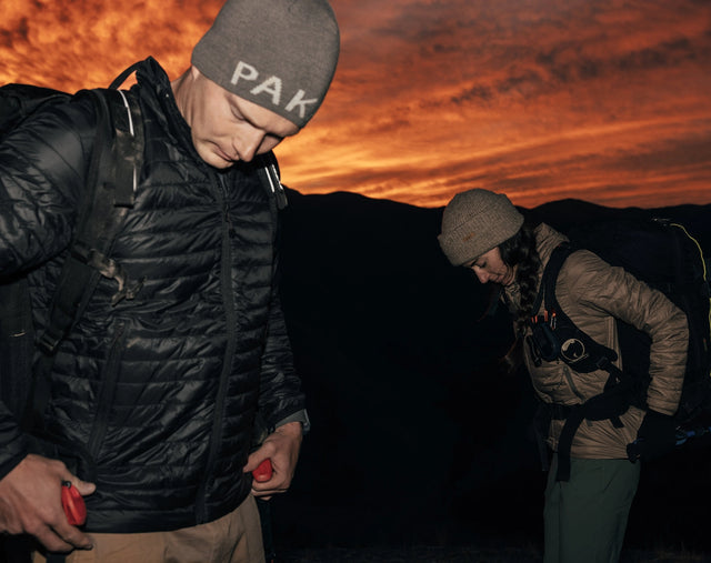 Three-quarter view of Mayu Ultralight jacket showing lightweight puffer quilting and hood against a sunset sky