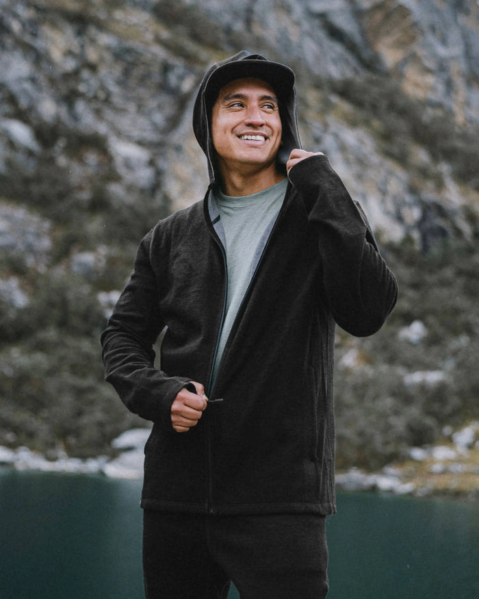 Man zipping black Men’s Breathe full-zip hoodie with hood up, slim athletic fit, standing by a mountain lake