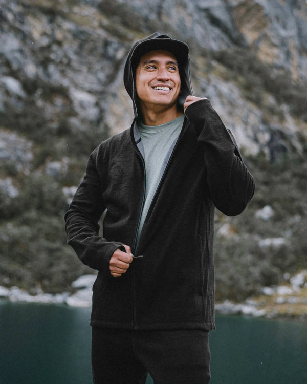 Man zipping black Men’s Breathe full-zip hoodie with hood up, slim athletic fit, standing by a mountain lake