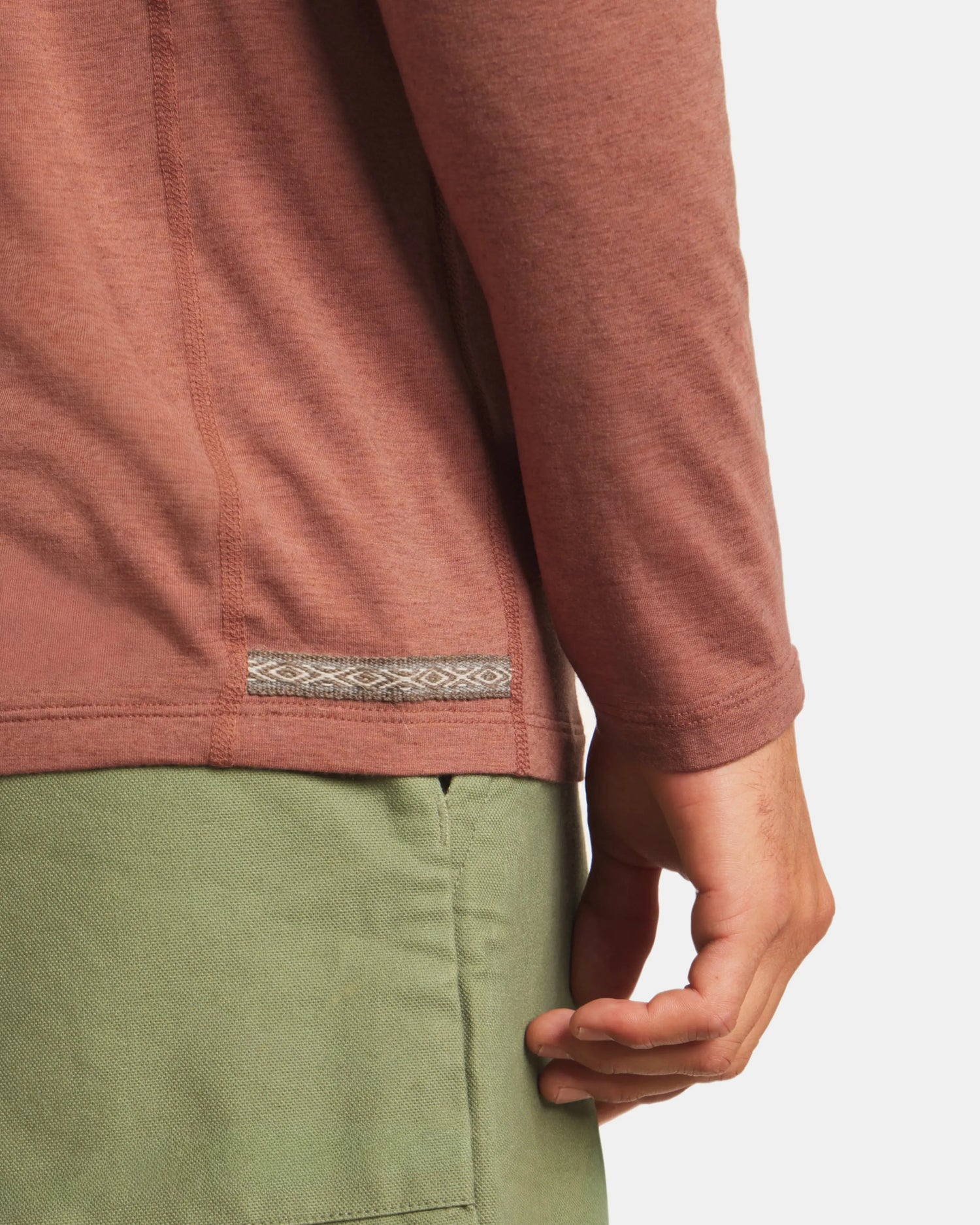 Close-up of Men’s Sol Crew long-sleeve alpaca shirt in cinnamon showing side seam, woven tab, and hem against light gray