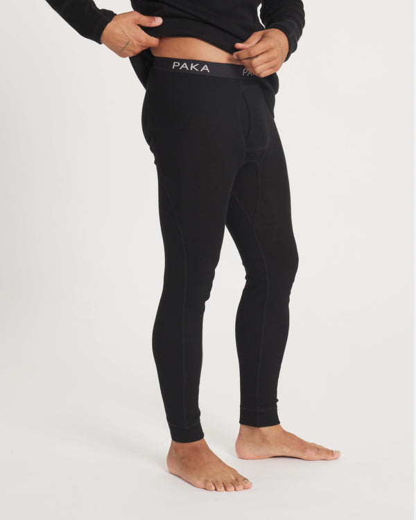 Side view of men’s alpaca thermal bottoms in black showing snug fit, seam detailing and PAKA waistband on light background