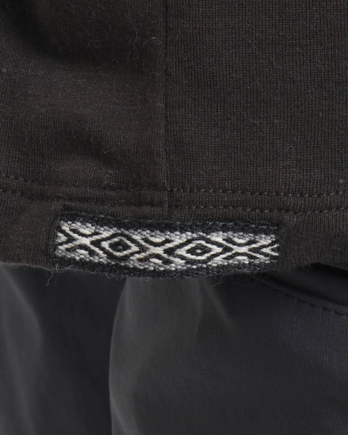 Close-up of hem of Men’s Aire Long Sleeve alpaca shirt showing black fabric and woven jacquard trim at the side seam