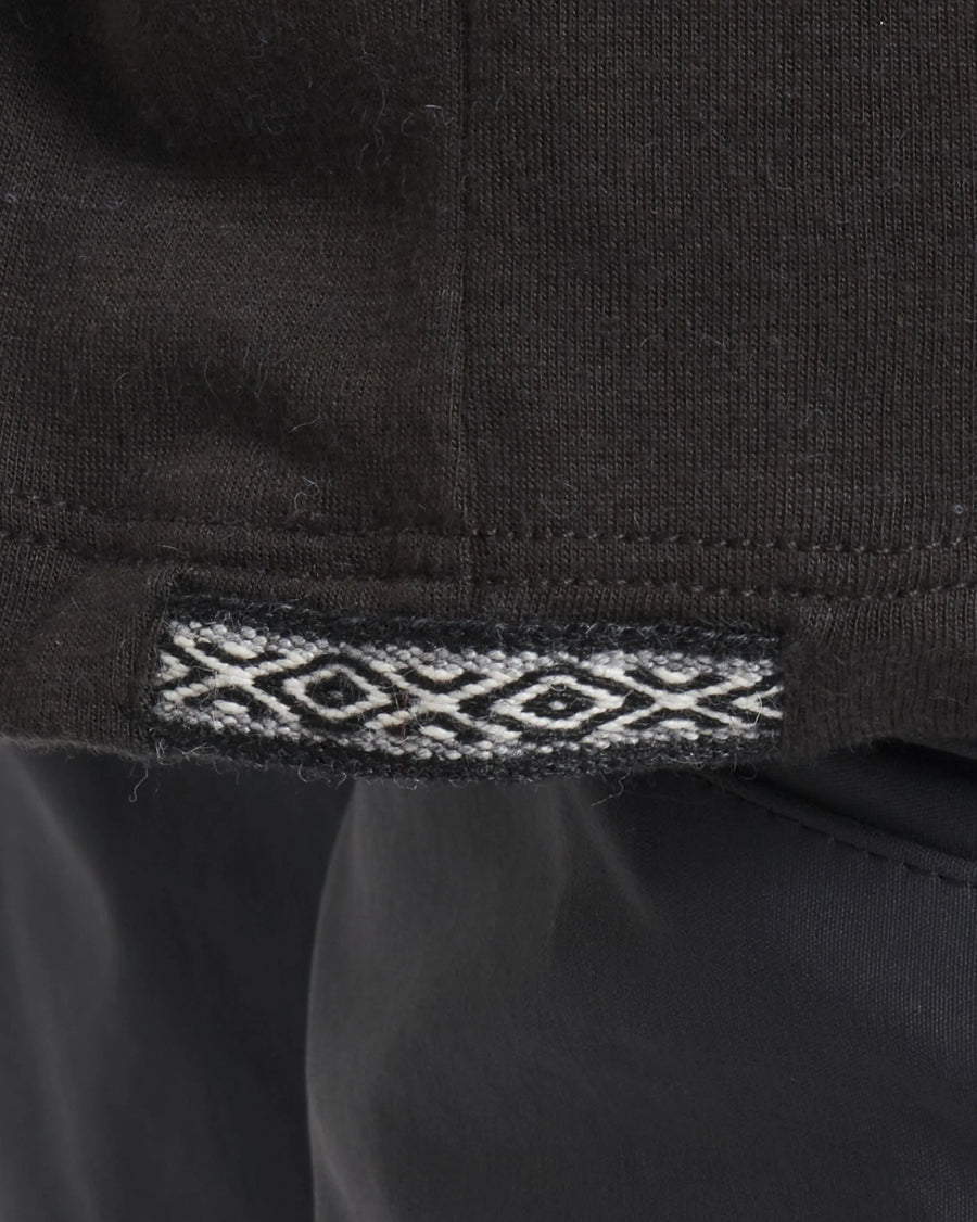 Close-up of hem of Men’s Aire Long Sleeve alpaca shirt showing black fabric and woven jacquard trim at the side seam