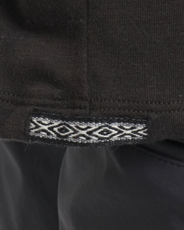 Close-up of hem of Men’s Aire Long Sleeve alpaca shirt showing black fabric and woven jacquard trim at the side seam