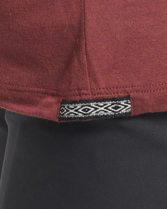 Close-up of Men’s Aire Long Sleeve shirt hem in clay showing woven geometric tag and center hem stitching against dark pants