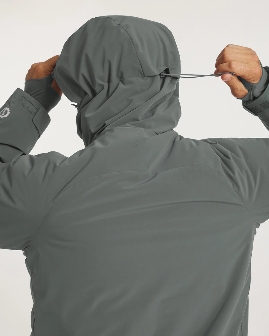 Rear view of Men’s Apu Parka in eucalyptus on model showing adjustable hood drawcord and waterproof shell on light background