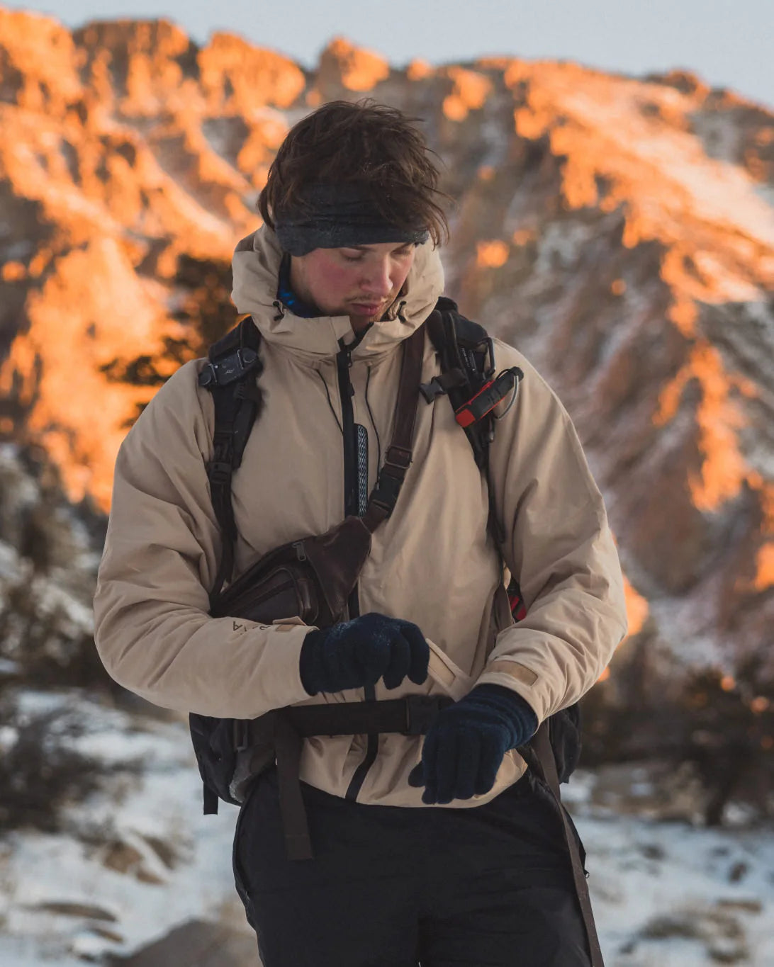 Man Tightening Wrist Strap on Puma / Tan Apu Parka Winter Jacket with Mountain in Background – PAKA Apparel