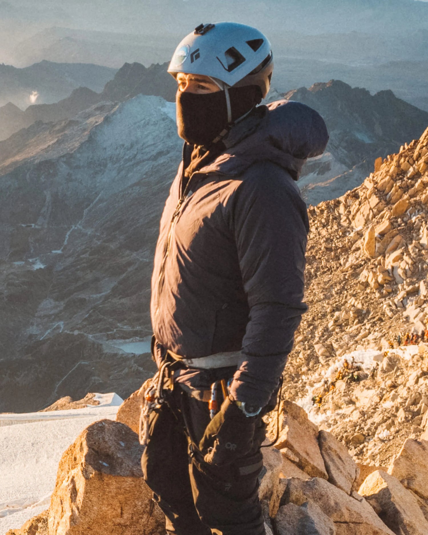 Three-quarter view of Men’s Apu Lightweight Puffer jacket showing hood and insulation on a climber at a rocky mountain summit