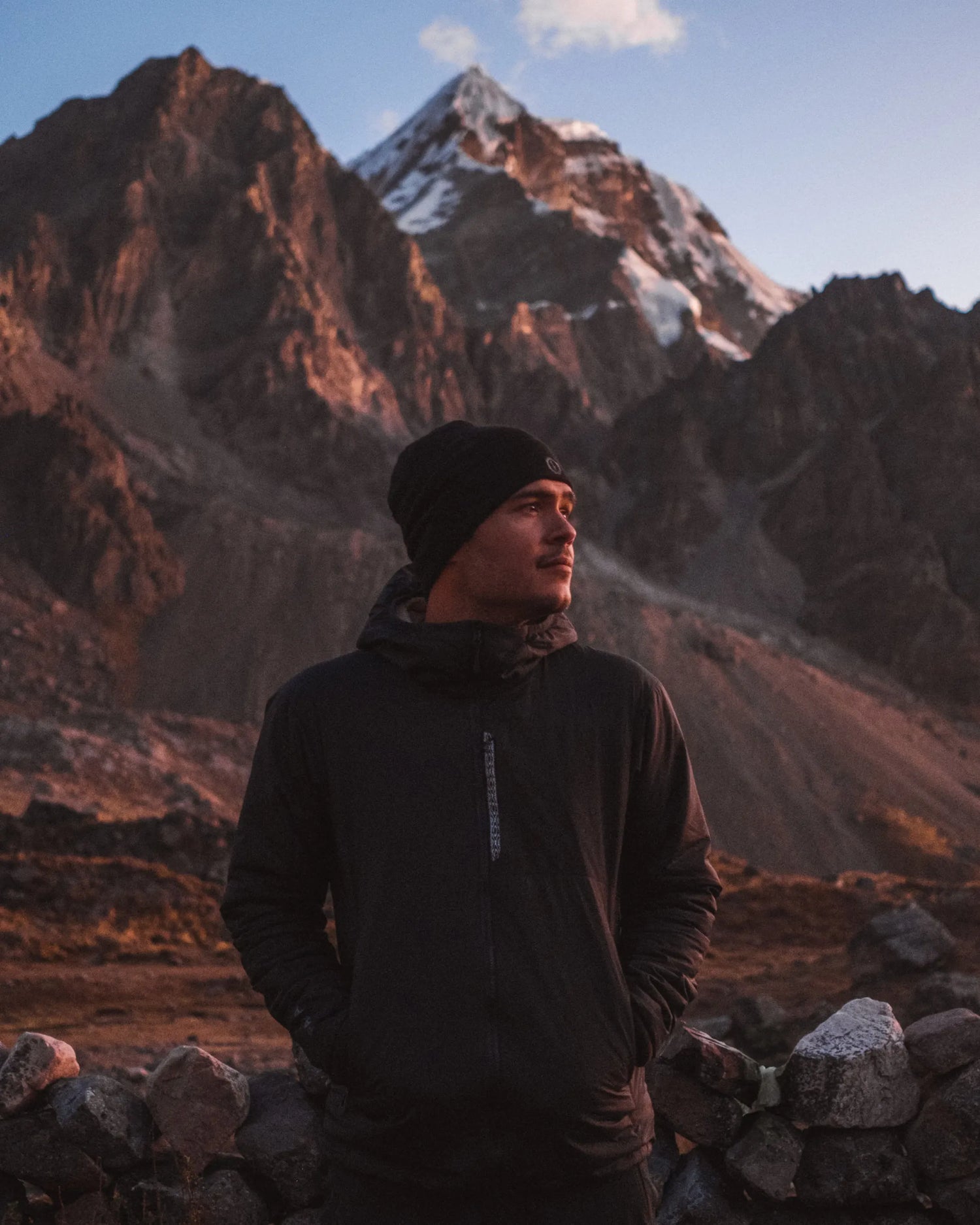 Front view of Men’s Apu Lightweight Puffer jacket with hood in black showcasing hood and chest zipper against mountain sunset