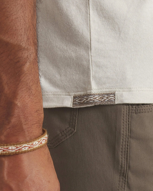 Side waist view of Men’s Essential Tee in bone showing woven Inca hem tag with model wearing olive pants