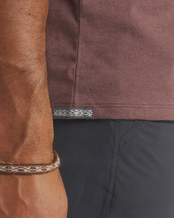 Side hem of men’s Essential Tee in mauve showing woven Inca ID tag and model’s wrist against dark pants