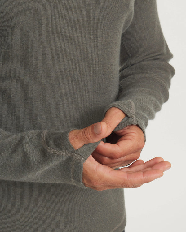 Close-up of men’s thermal hoodie sleeves in Andean Moss showcasing thumbholes, flat coverstitch seams and ribbed knit on a light background