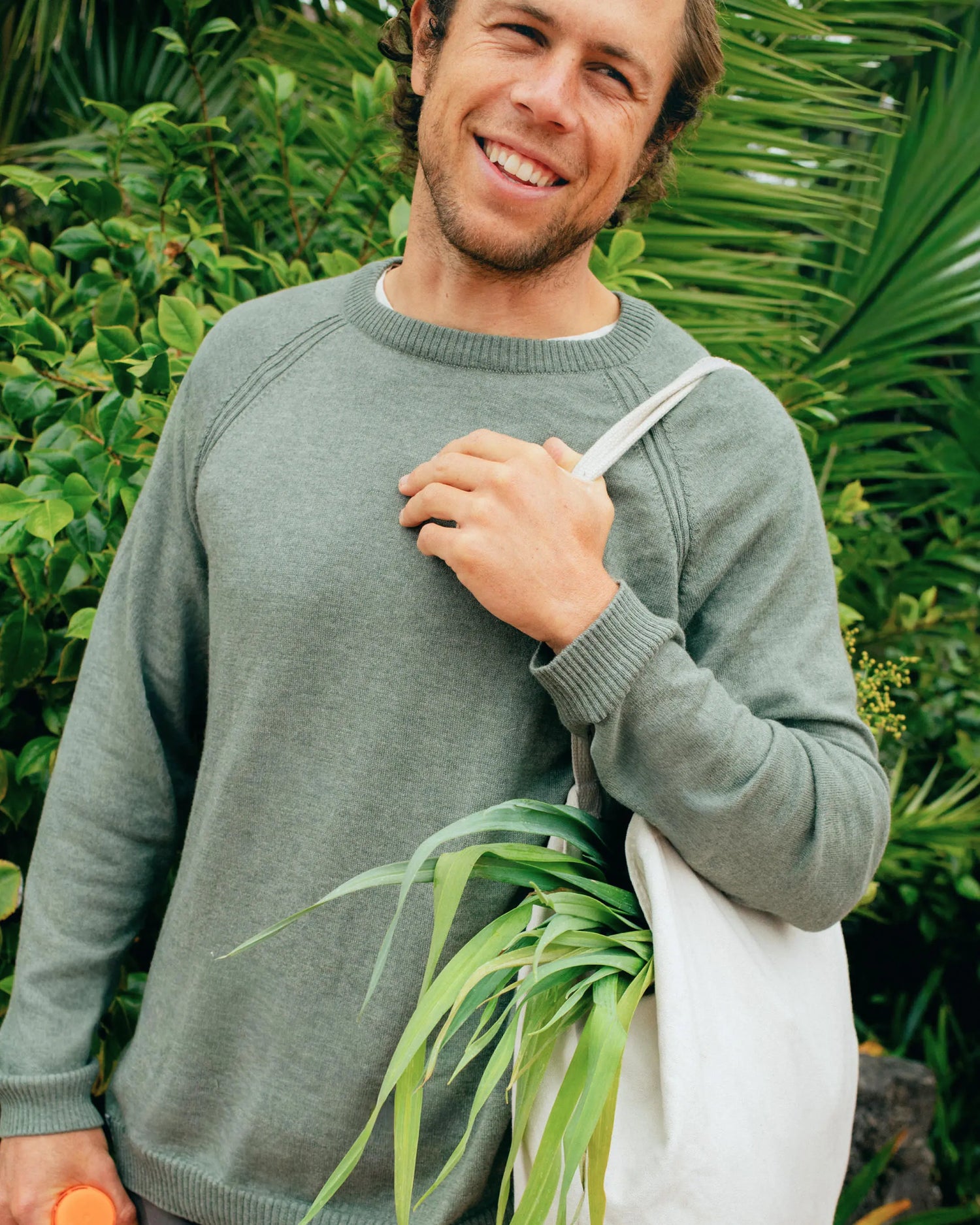 Man holding a plant against a green leafy background