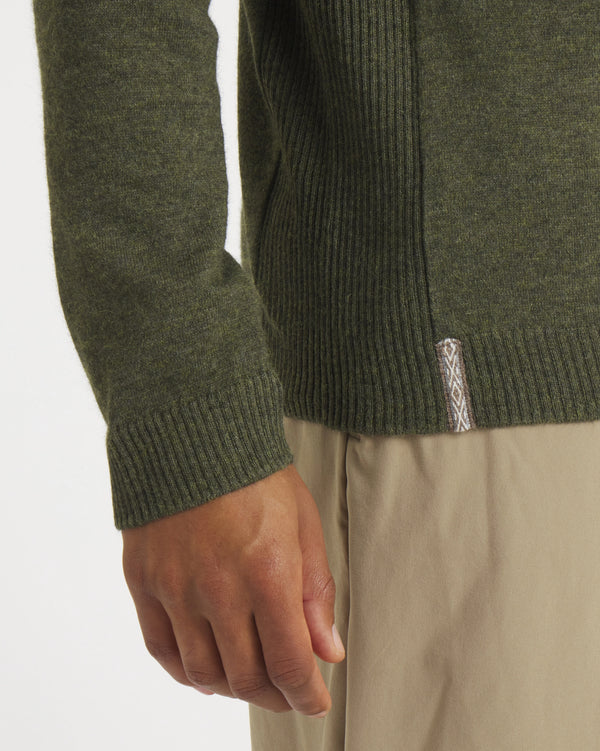 Close-up of Men’s Ultralight 1.0 Crew in Andean Moss showing ribbed sleeve cuff and hem, alpaca fabric texture, and woven side tag on a light background