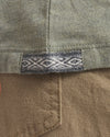 Close-up of Men’s Essential Tee showcasing woven Inca ID hem tag and knit fabric texture with tan pants pocket background