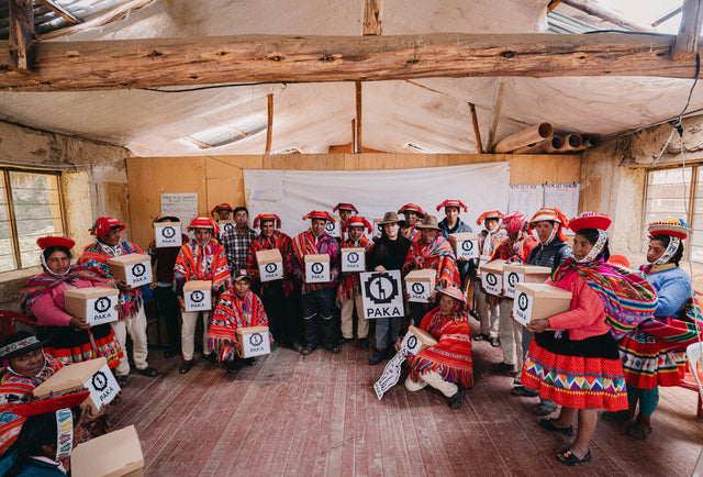 Peruvian weavers and community members gathered in a workshop displaying finished textiles and smiling