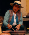 Woman dyeing yarn in a bowl inside a workshop, wearing a straw hat and blue sweater