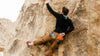 Man bouldering on a granite boulder wearing a black zip hoodie and brown pants with an orange chalk bag