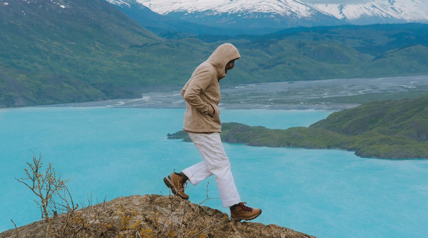 Person wearing cream zip hoodie standing on a rock overlooking a turquoise mountain lake