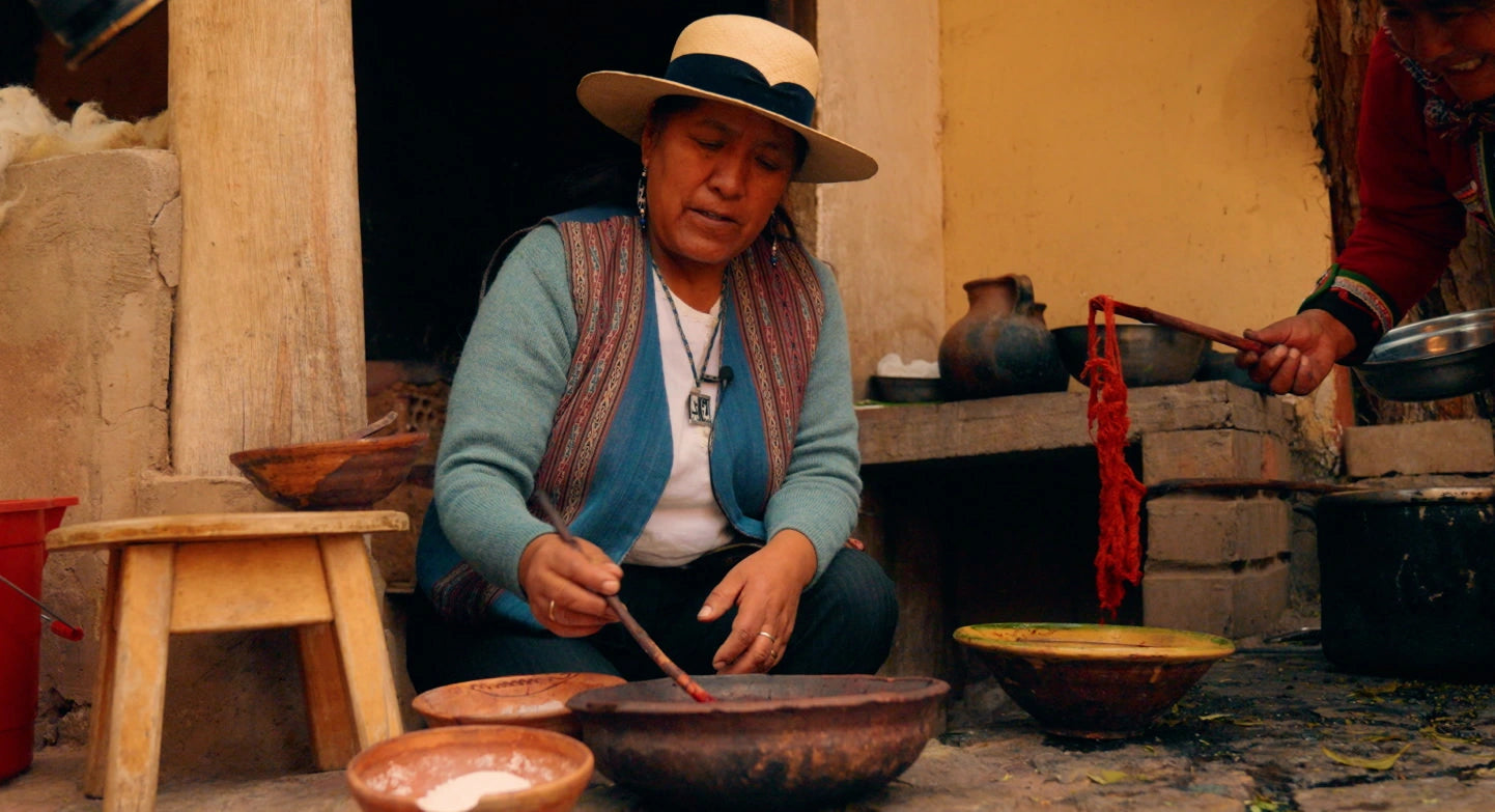 Quechua woman stirring natural dye in clay bowls and lifting red dyed yarn outside a traditional home in Chinchero, Peru