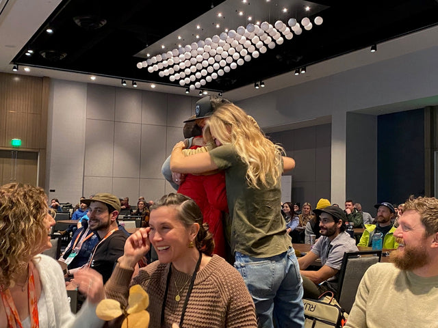 Paka team members hugging and celebrating in a conference room with seated audience