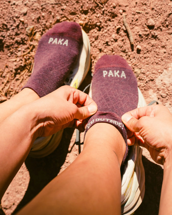 Top-down view of Trail Ankle Socks on feet showing low-cut ankle fit, PAKA logo, and textured trail background