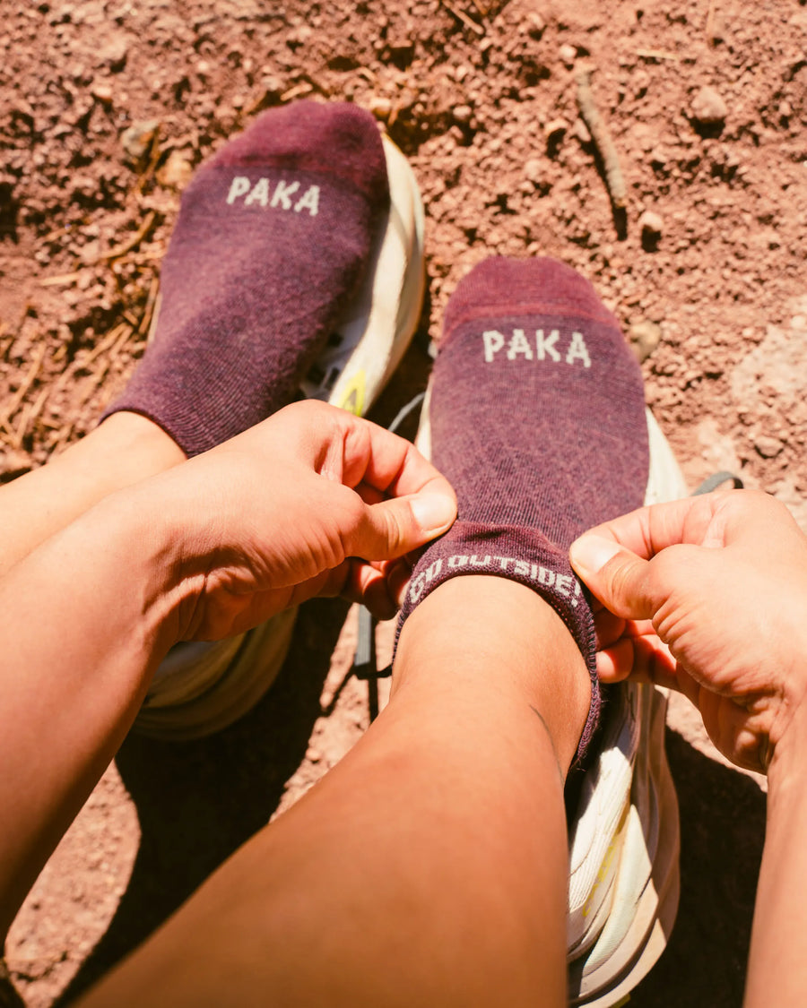 Top-down view of Trail Ankle Socks on feet showing low-cut ankle fit, PAKA logo, and textured trail background