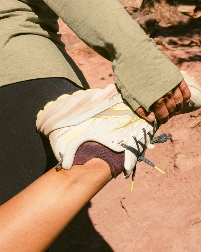 Person pulling on purple ankle alpaca socks while trail running on a red dirt path