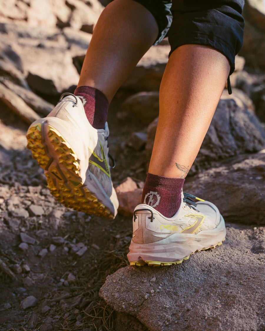 Hiker’s lower legs stepping on rocky trail wearing maroon Trail 1/4 Crew Socks and light trail shoes