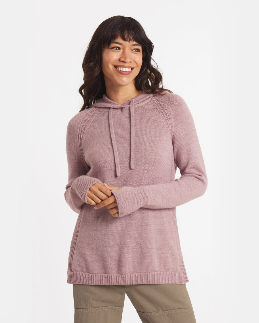 Three-quarter view of alpaca hoodie in dusty rose showing hood with drawstrings, raglan sleeves, and relaxed fit on model