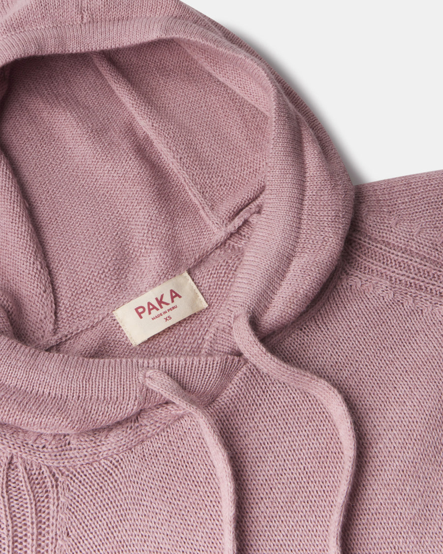 Close-up of women’s alpaca hoodie showing hood, drawstrings, knit texture, and PAKA label on pale gray background