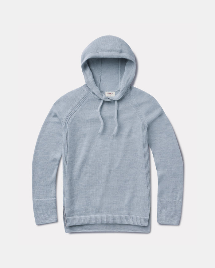 Flat lay of light blue women’s alpaca hoodie showcasing hood, drawstrings, raglan seams and ribbed cuffs on pale gray background