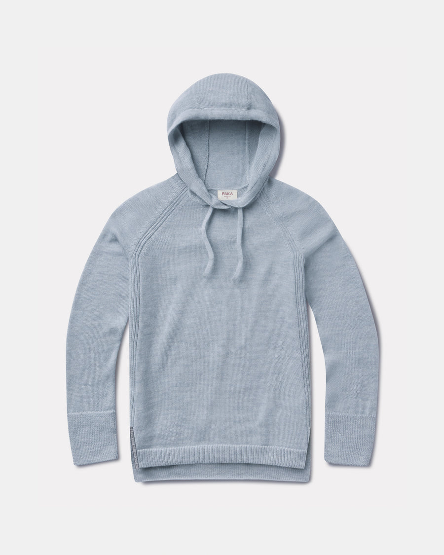 Flat lay of light blue women’s alpaca hoodie showcasing hood, drawstrings, raglan seams and ribbed cuffs on pale gray background