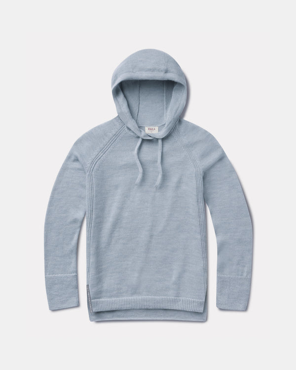 Flat lay of light blue women’s alpaca hoodie showcasing hood, drawstrings, raglan seams and ribbed cuffs on pale gray background