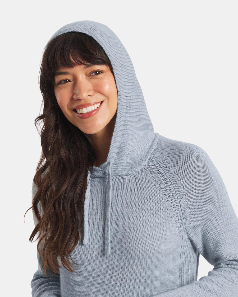 Three-quarter view of women’s light blue alpaca hoodie on model, hood with drawstrings, relaxed fit, light gray background
