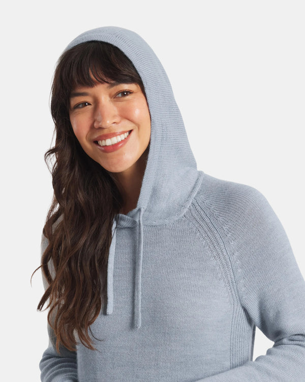 Three-quarter view of women’s light blue alpaca hoodie on model, hood with drawstrings, relaxed fit, light gray background