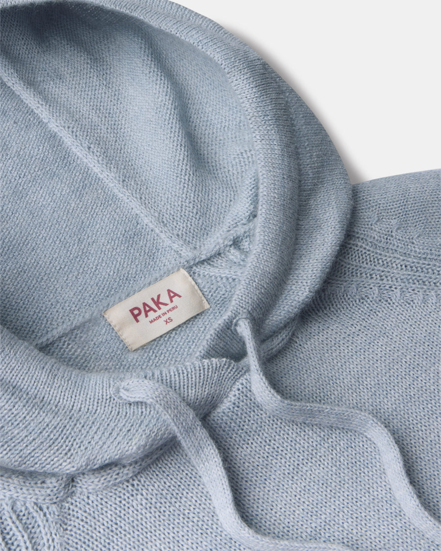 Close-up of women’s light blue alpaca hoodie showcasing hood, drawstrings, soft knit texture, and PAKA label on light gray background
