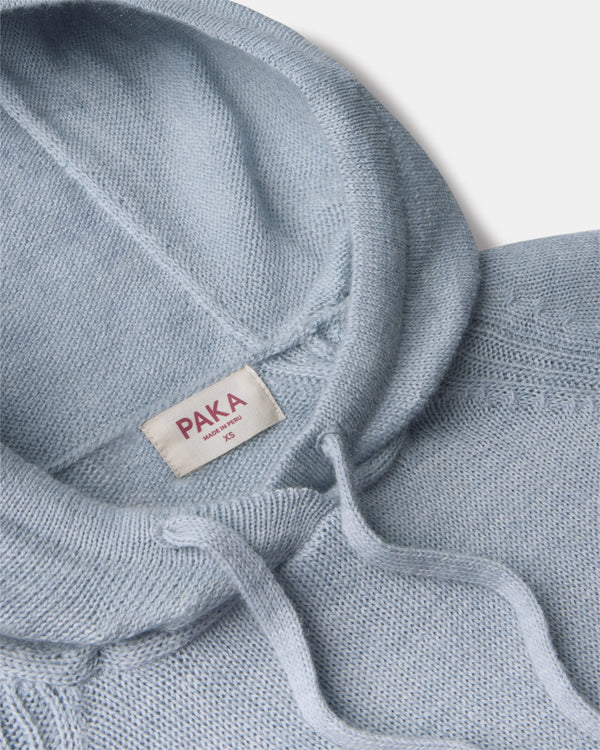 Close-up of women’s light blue alpaca hoodie showcasing hood, drawstrings, soft knit texture, and PAKA label on light gray background