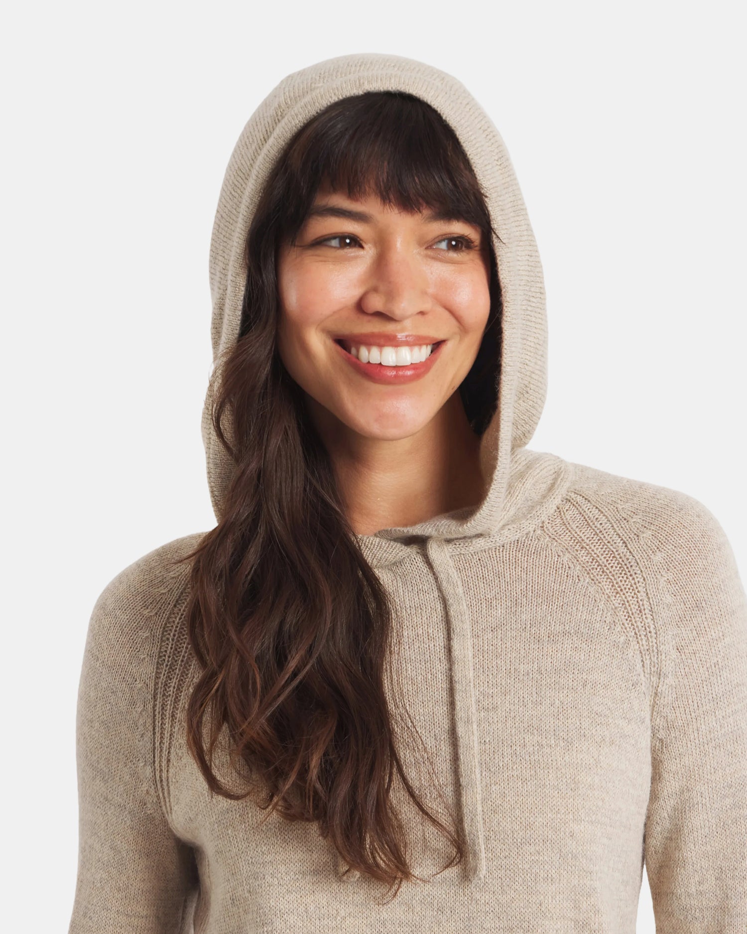 Front close-up of women’s alpaca hoodie in light beige on a smiling model, showing hood with drawstring and soft knit texture