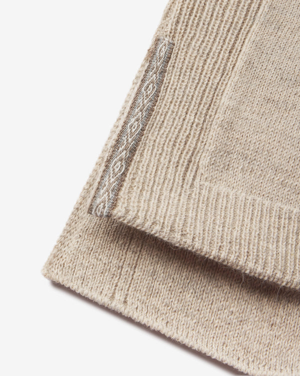 Close-up of women’s alpaca hoodie hem showcasing ribbed knit texture and decorative woven side seam tag on white background