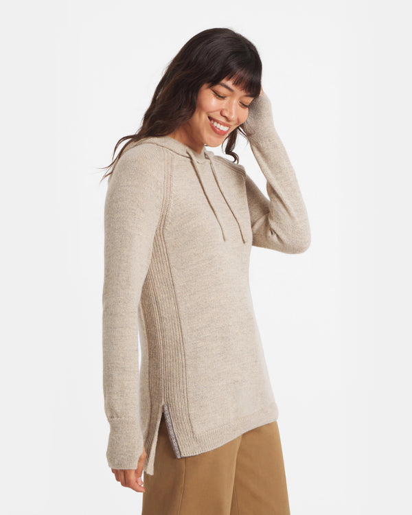 Side view of oatmeal alpaca hoodie showing ribbed side panels, longline tunic fit, drawstring hood on a smiling model