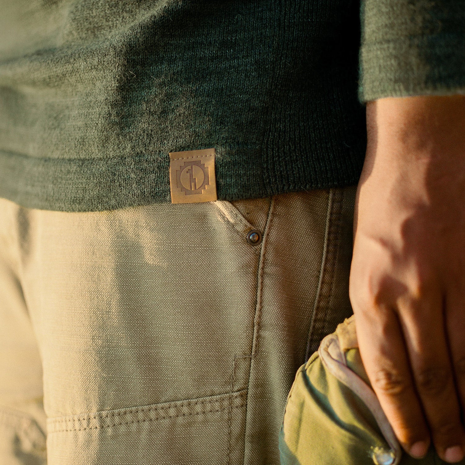 Close-up of The Original Crew alpaca crewneck hem showing soft knit texture and leather PAKA logo tag over beige pants