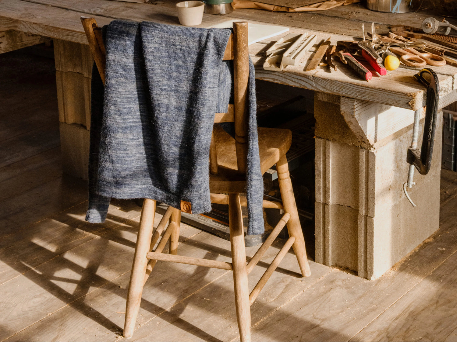 Angled view of The Original Crew alpaca crewneck showing heather blue knit and leather hem tag draped on a wooden chair