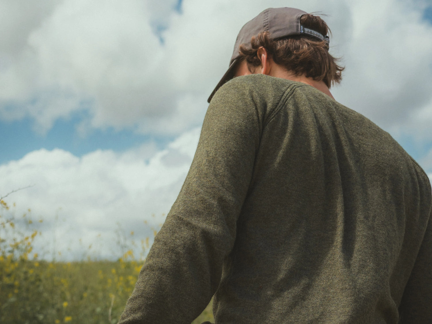 Rear view of Men’s Ultralight 1.0 Crew (olive) showing knit texture and raglan seam on model against cloudy sky
