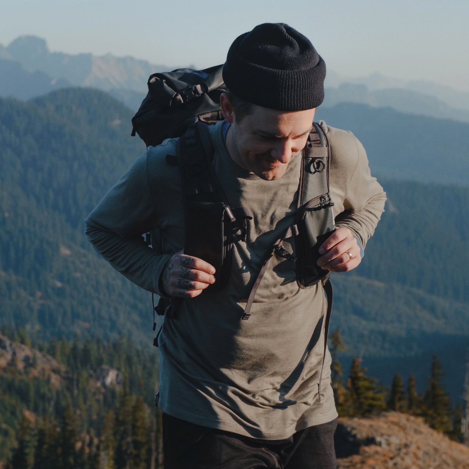 Hiker adjusting a backpack while wearing an Andean Moss Men’s Aire long sleeve shirt, slim fit, mountain backdrop