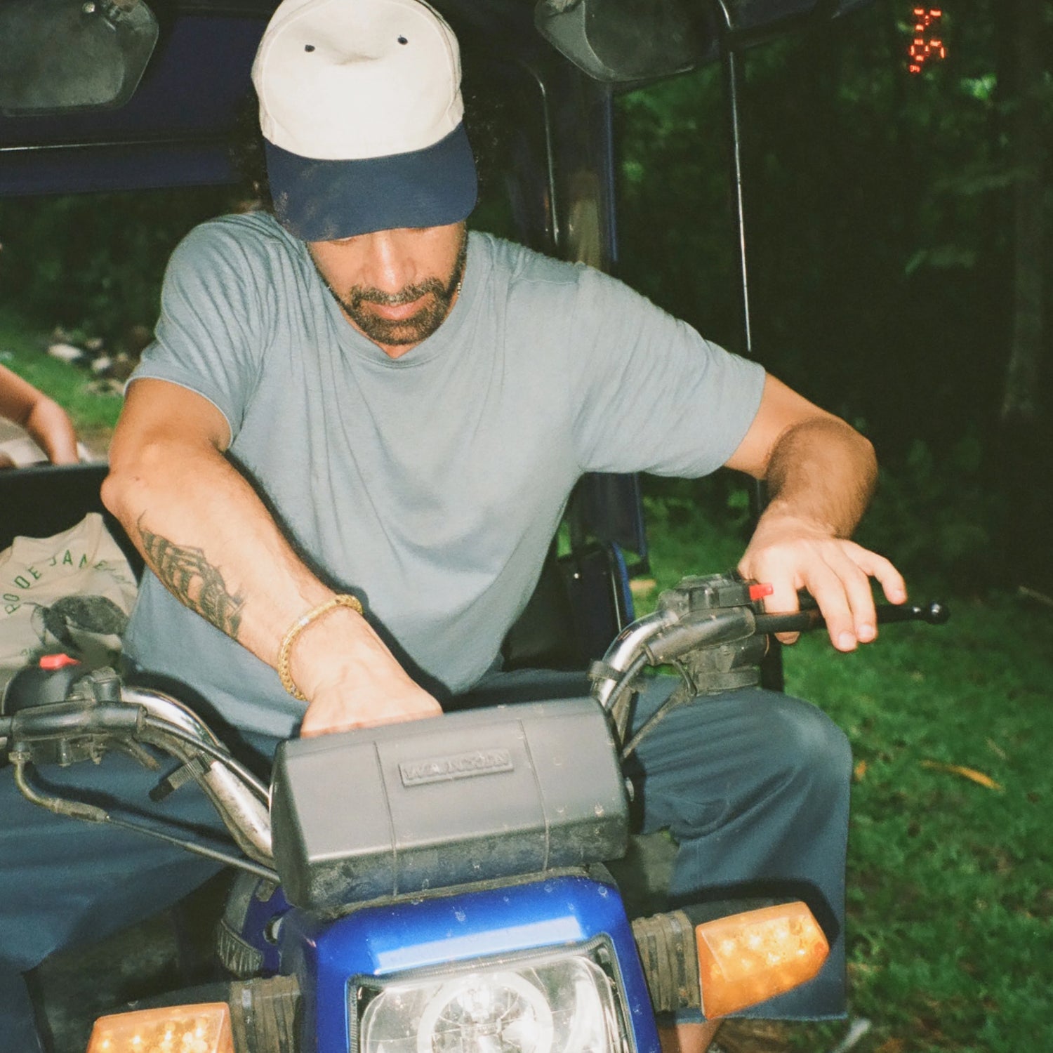 Man wearing light blue Men’s Essential Tee, relaxed fit, leaning forward on an ATV in a shaded outdoor setting
